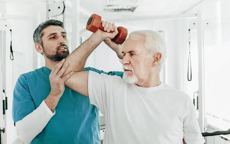 An older adult lifting a light dumbbell while an expert supports the arm