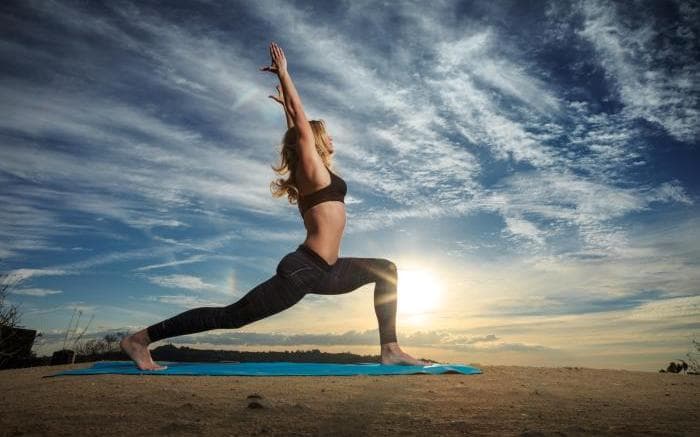 A woman holding a standing lunge on an exercise mat outdoors at sunrise
